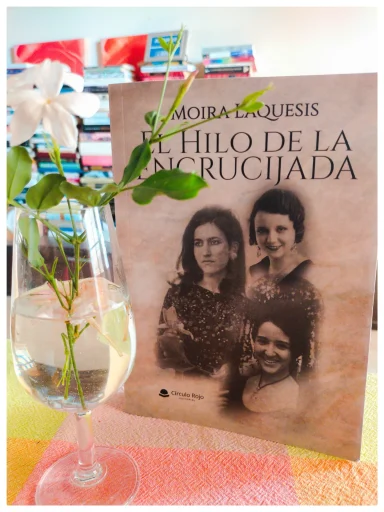 En casa se lee a Mora Láquesis La portada del libro "El Hilo de la Encrucijada" de Moira Láquesis junto a una copa con flores.