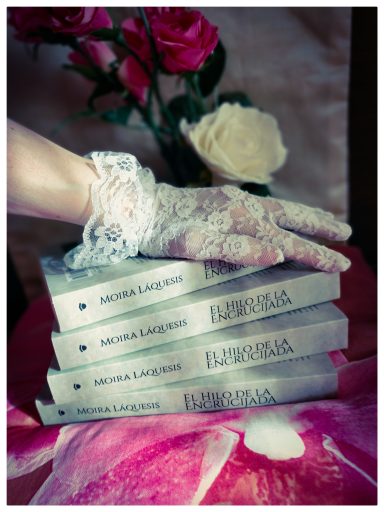 Mi obra Cuatro libros apilados de "El hilo de la encrucijada". Una mano enguantada con encaje, descansa encima.